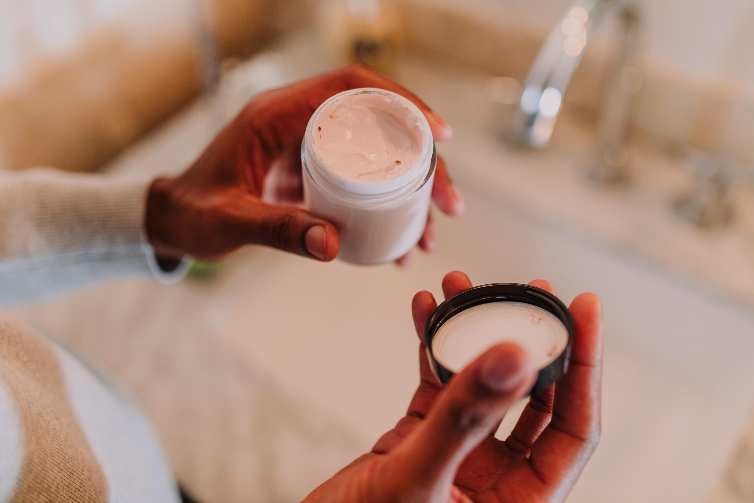 High angle view of hands holding a moisturizer jar next to a bathroom sink.